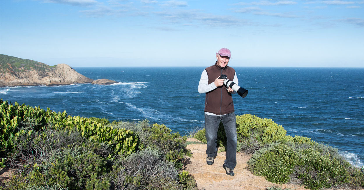 Richard Du Toit, fine art nature and wildlife photographer holding his camera on location on the African coastline. Richard Du Toit photography and artwork is available at Sarza store home goods, wall art and furniture store.